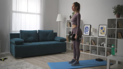 sportswoman-is-holding-dumbbells-in-hands-and-doing-tilts-training-at-home-full-length-shot-in-living-room-caring-about-body-health-and-beauty